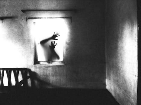 Eerie silhouette of hands pressed against a window in a dark room, evoking mystery and suspense.