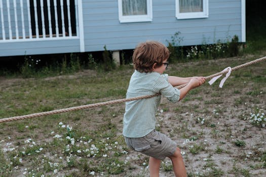 Young boy engaged in a tug of war outside near a blue building during the day.