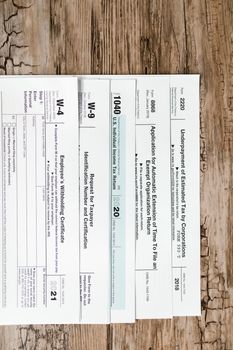 Close-up of various U.S. tax forms including W-4, W-9, and 1040 on a rustic wooden surface.